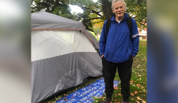 Phil, an encampment resident at Allan Gardens Park, stands next to a sign behind his tent which reads “It is not over, it’s only just beginning. It’s not about revolution, it’s about solutions and becoming one again. It’s a new beginning. Start your own community, build your own home.”