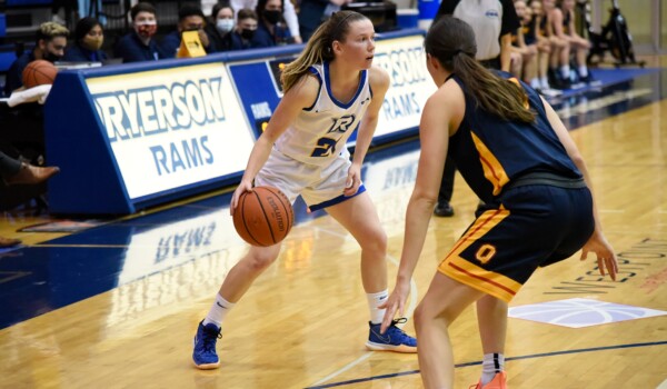 A woman in a white and blue basketball uniform dribbles a ball on a court during a game.